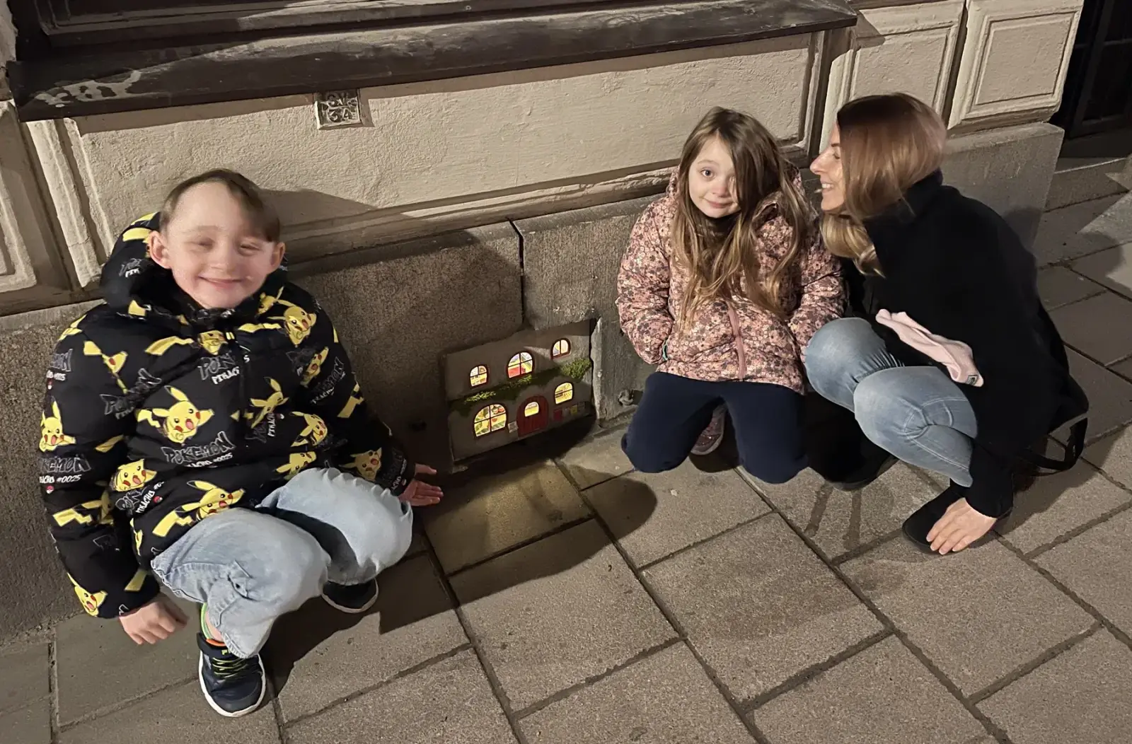 Bambini e un adulto accovacciati accanto alla casa in miniatura di Bamse in Södermalm