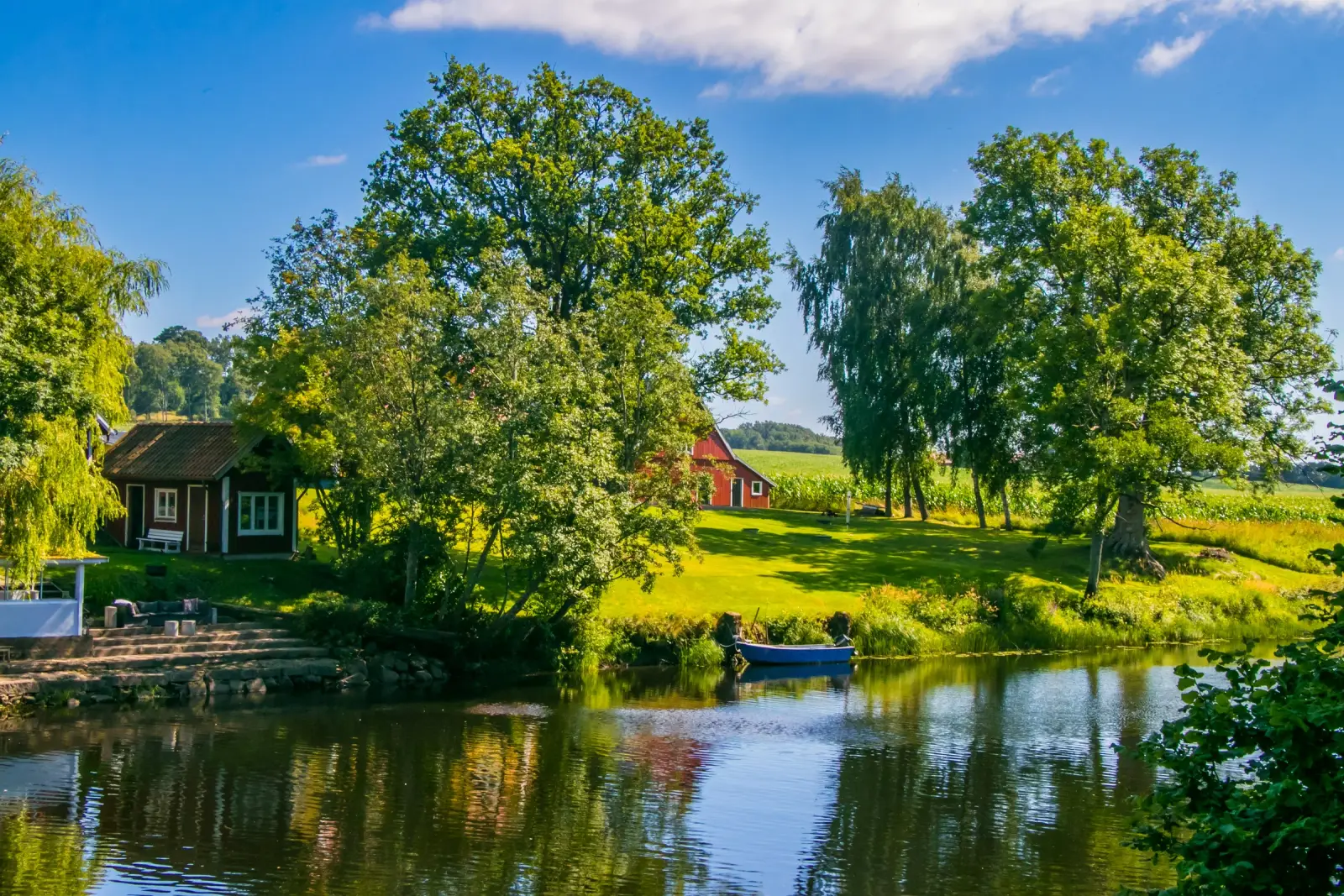 Rivage calme de l'archipel avec des arbres, des cottages rouges et un petit bateau sur l'eau